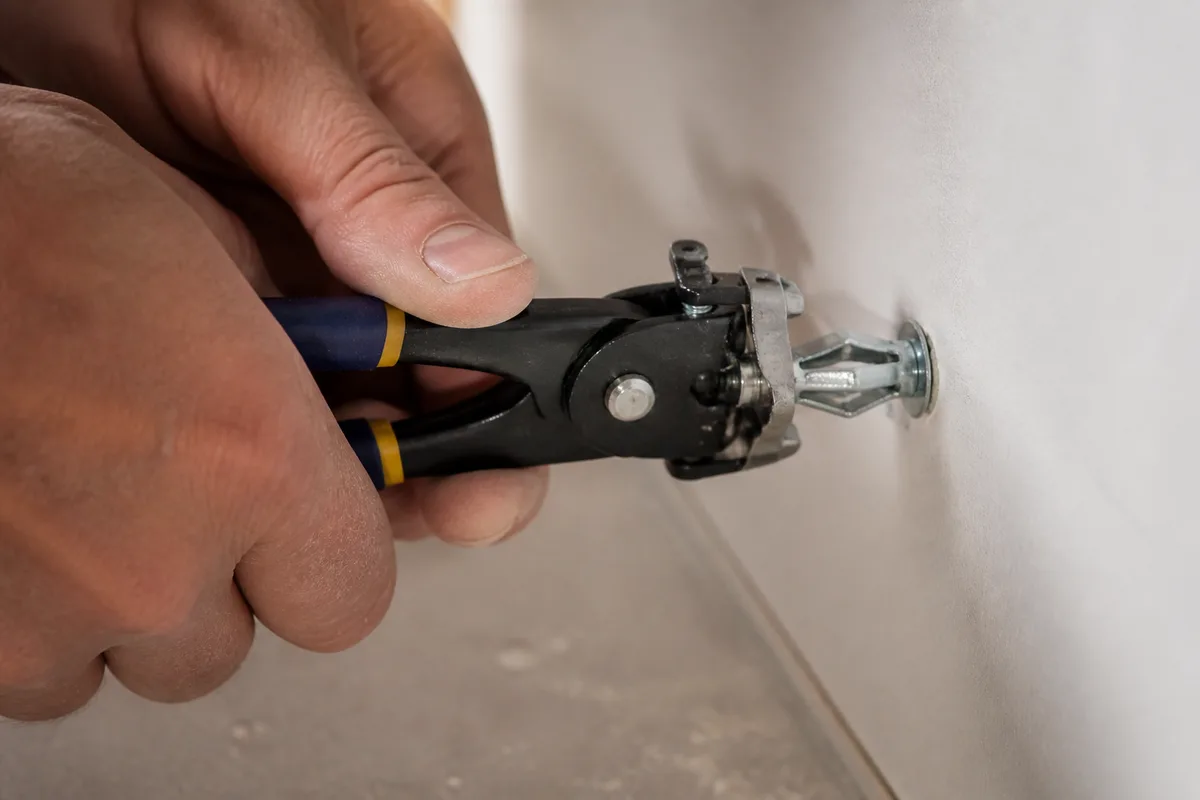 Mains posant une cheville métallique à expansion dans une plaque de plâtre avec une pince
