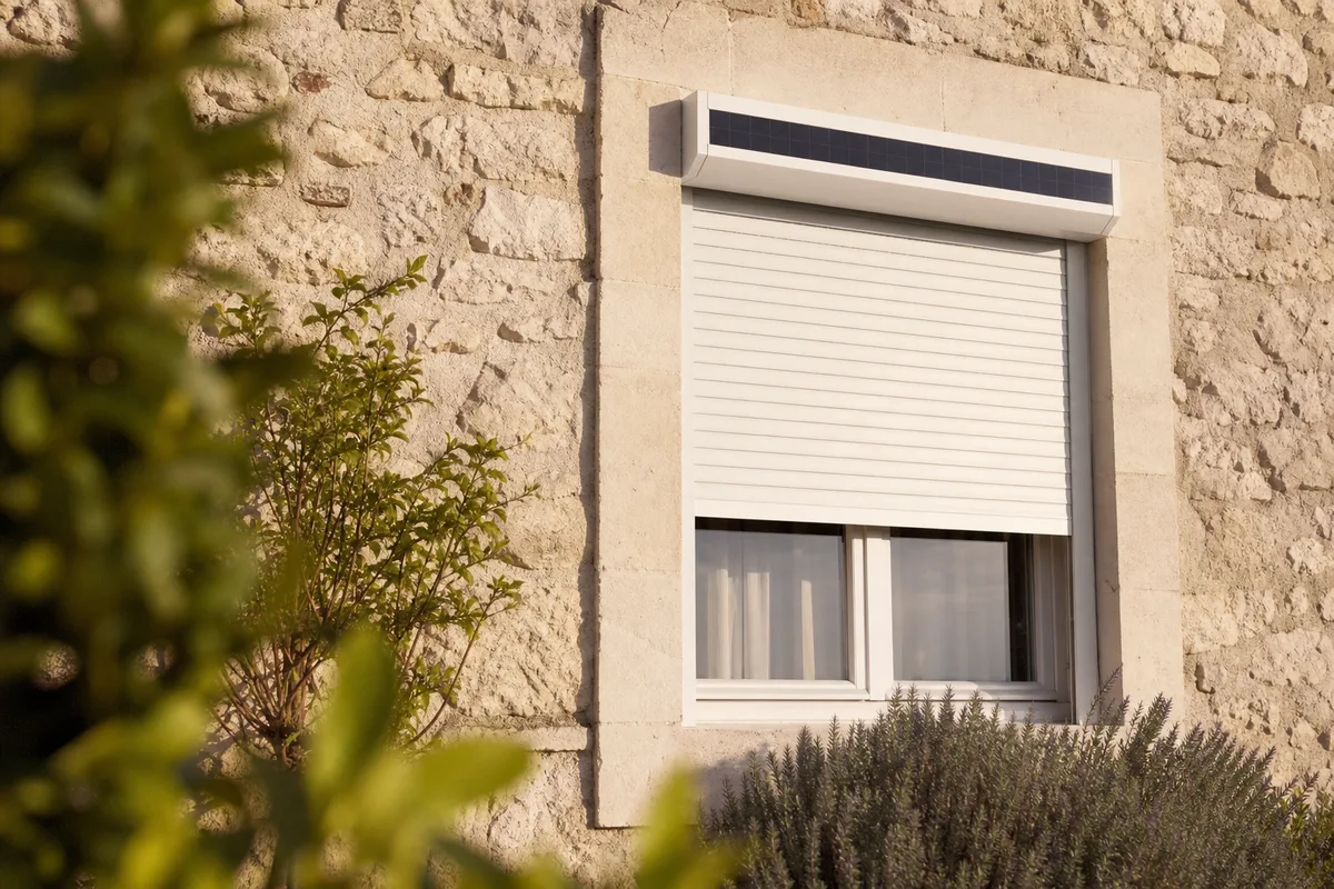 Panneau solaire intégré au coffre d&rsquo;un volet roulant sur une façade en pierre